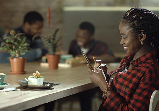 young woman typing on her cellphone with a piece of cake sitting in front of her on a table