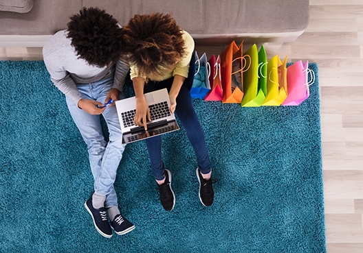 two people sitting on a carpet looking at a laptop