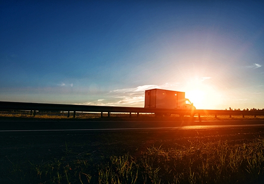 truck driving on a long rose as the sun rises