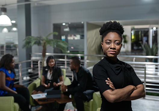 woman standing with her arms crossed in front of a group of people sitting around a table