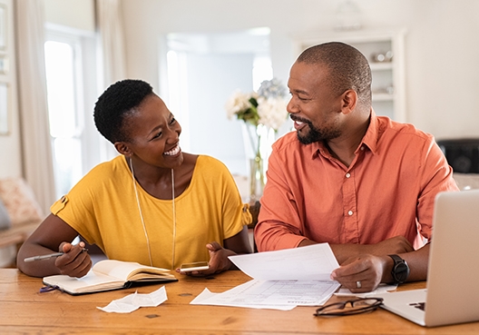 couple sitting at a dining table with their expenses spread out before them smiling at each other