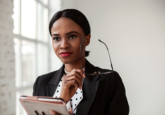A lady standing in thought while holding her spectacles