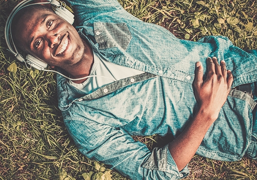 A man lies in the grass on his back and listens to music.