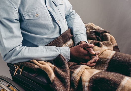 A man sitting in a wheelchair with a blanket covering his legs