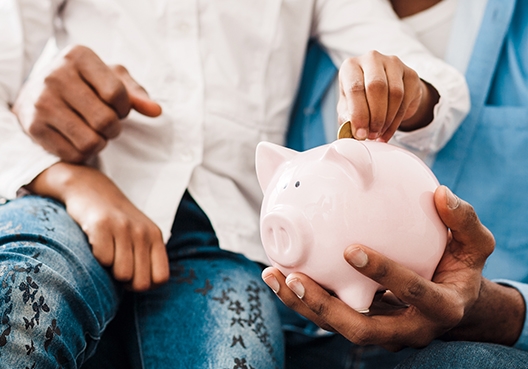father sitting with his daughter on his lap holding her piggy bank