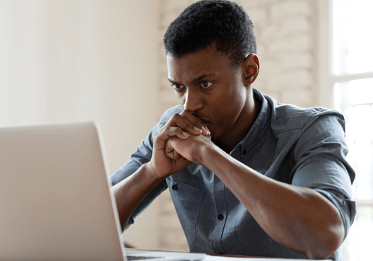 A man sitting worriedly at his desktop looking at his laptop