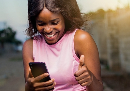 a young girl looking at her cellphone smiling with a thumbs up