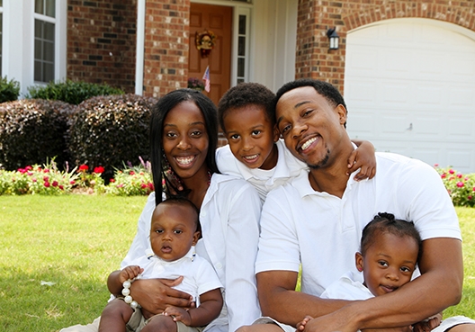 Family sitting on the lawn in front of the house looking at the camera