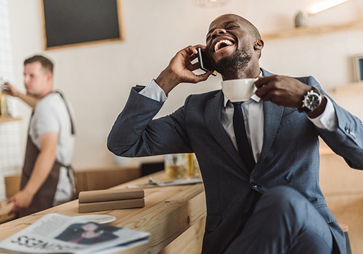 business man holding a cup of coffee while talking on his cell phone