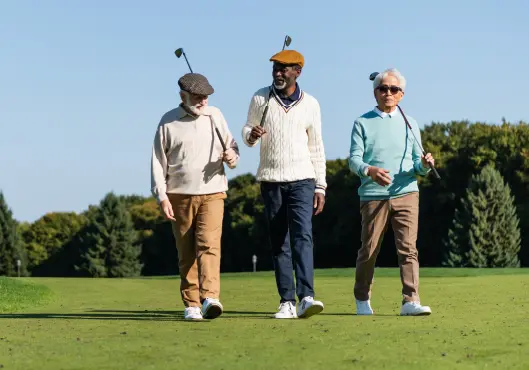 Three friends walking with golf clubs on green field